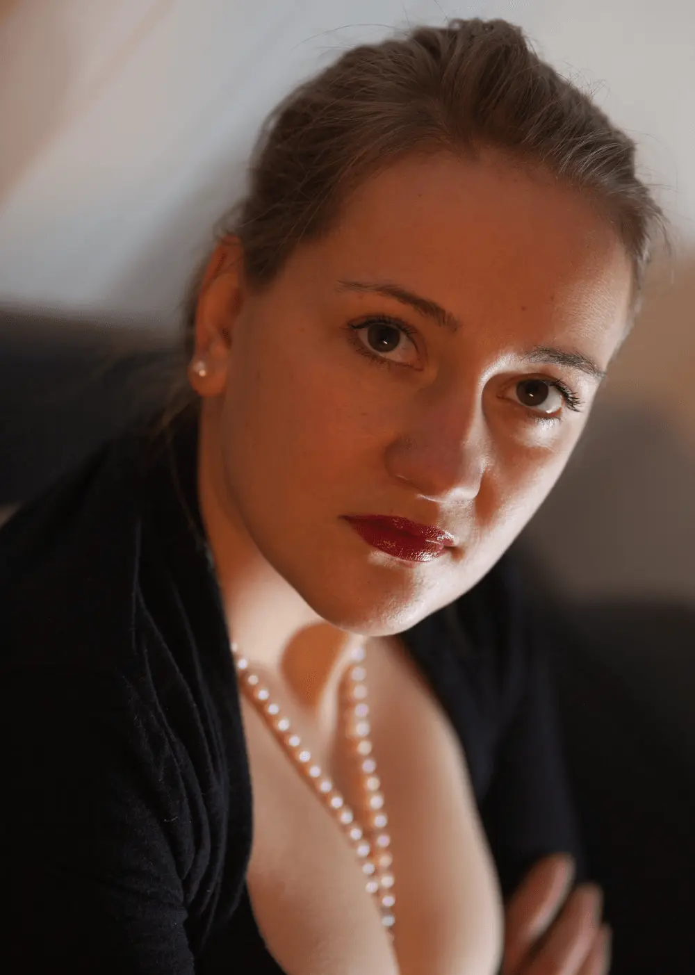 Portrait einer Frau mit Perlenkette, nach vorn geneigt, warmes Licht